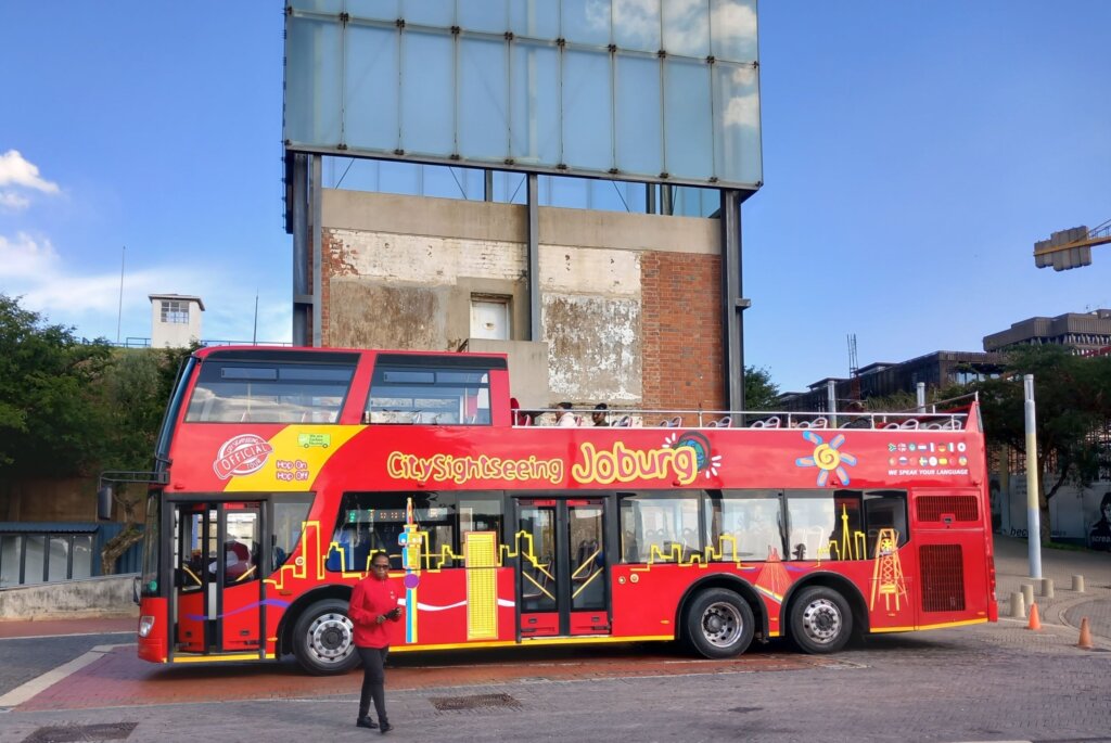 This photo shows a big red City Sightseeing bus parked in front of a watch tower on Constitution Hill