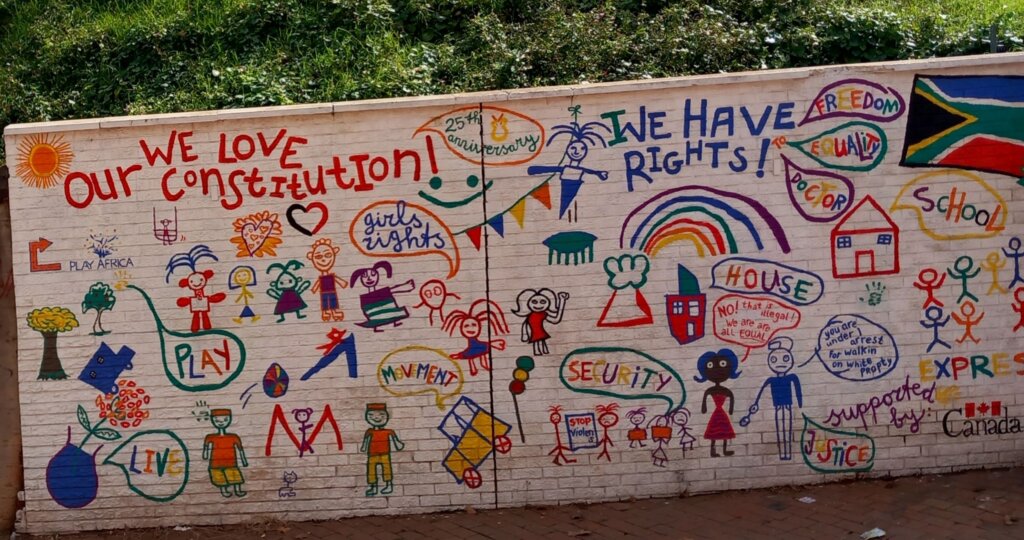 This image shows a wall covered in colourful graffiti which is on display at Constitution Hill