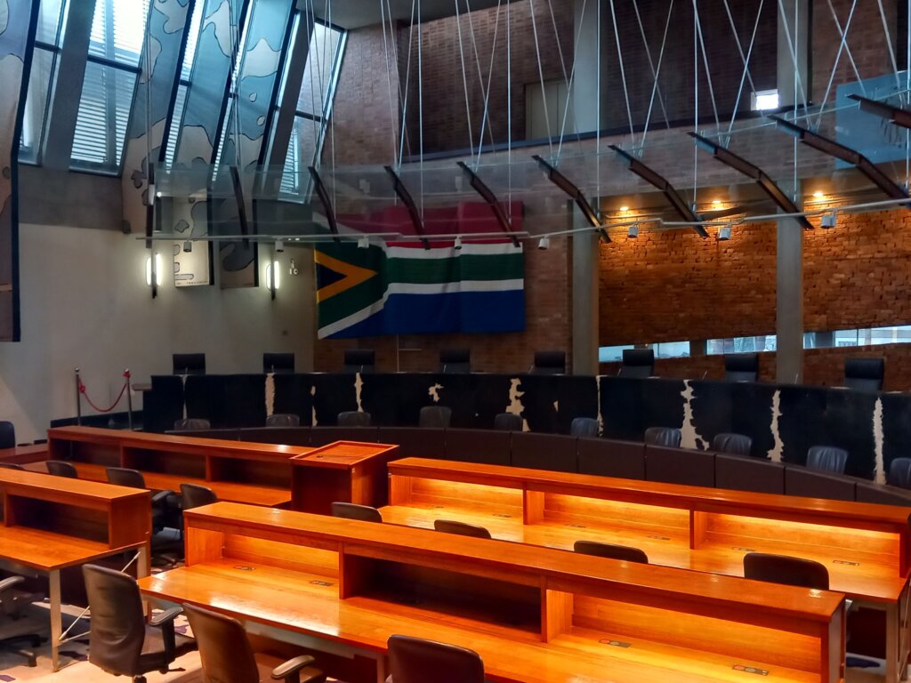 This photo shows the judges seats in the court room with the hand-stitched flag of South Africa hanging behind