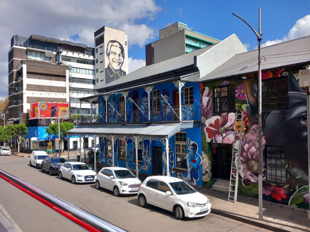 This image, taken from the top of a City Sightseeing bus, shows a street in downtown Johannesburg with a mural of Nelson Mandela painted on the side of a building