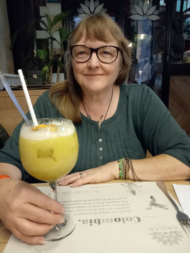 This photo shows Andrea with a large glass of lulada, a yellow drink with ice, a straw, and a mixing spoon in it